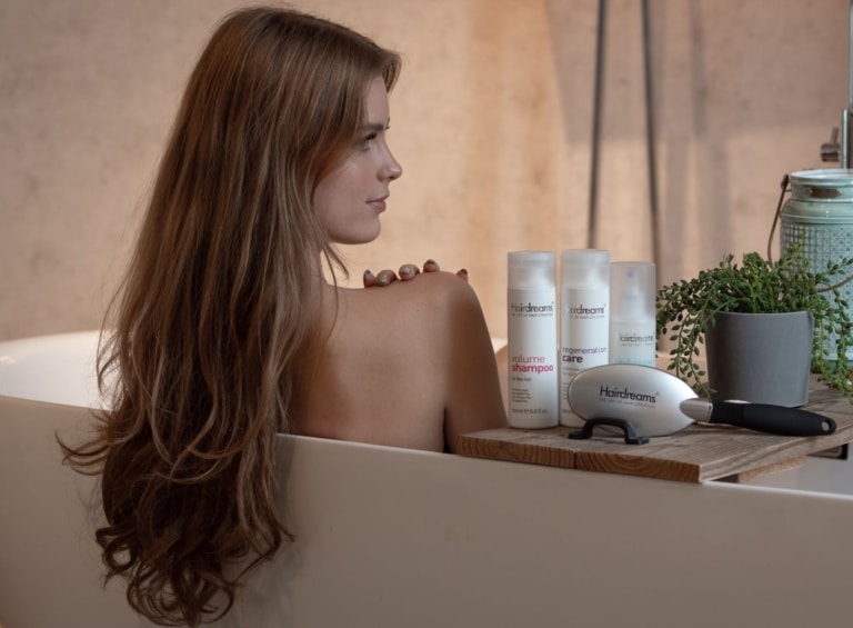 Woman sitting in the bathtub with her hair loose, Hairdreams hair care products next to her.